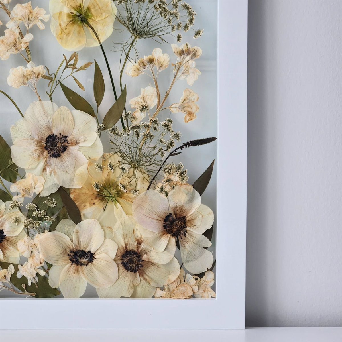 Pressed dried cream and yellow flowers arranged inside a white picture frame.