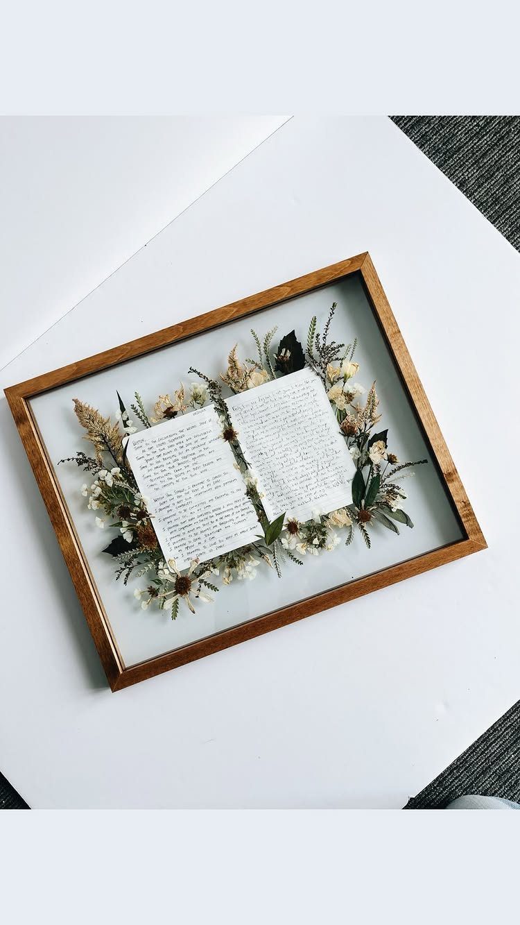 Framed open book with handwritten vows surrounded by dried flowers and greenery.