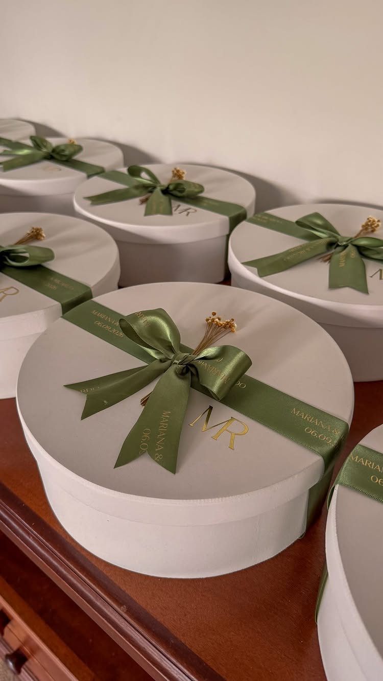 White round gift boxes with green ribbons and gold monogrammed initials on lids.