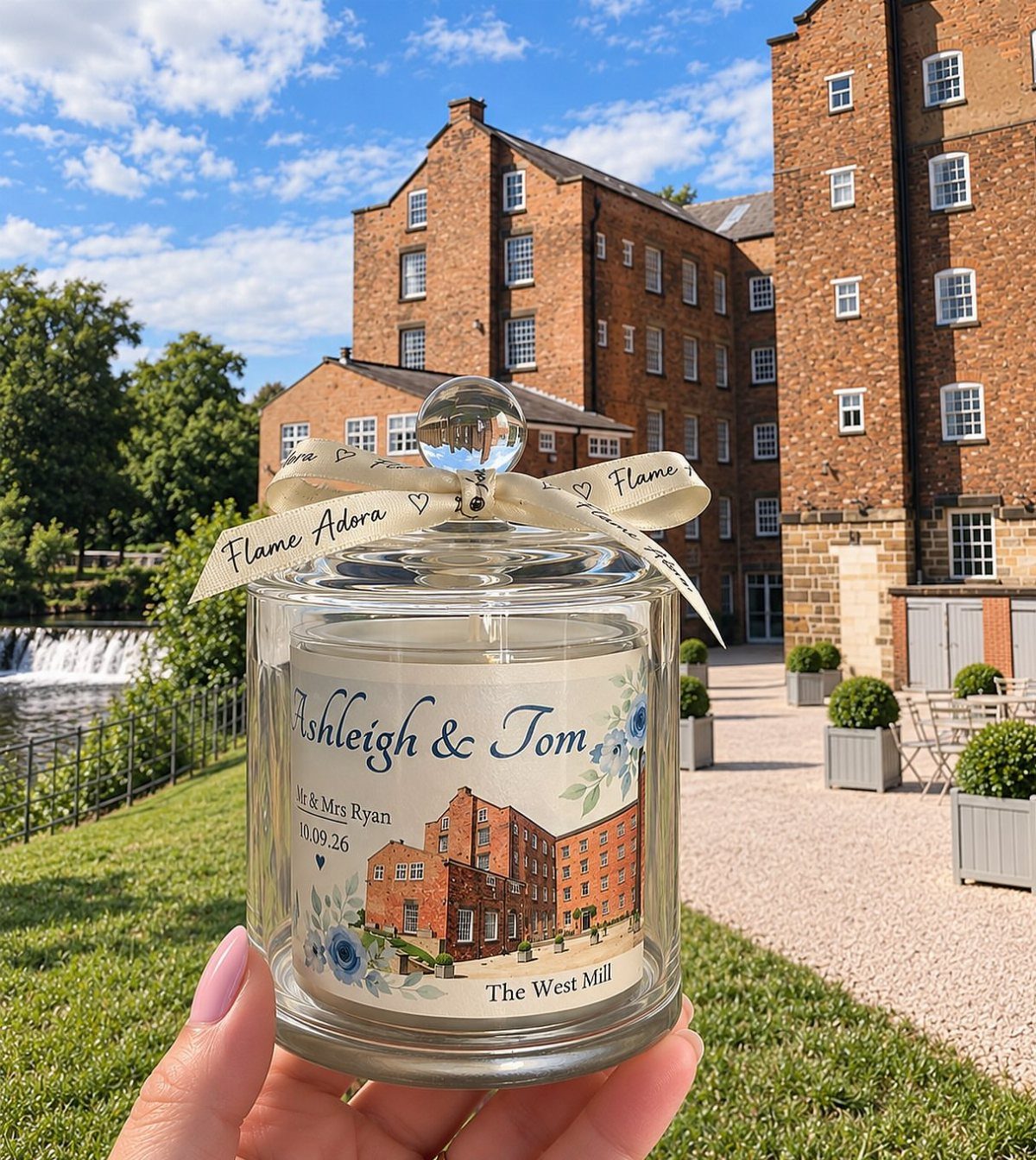 Personalized wedding candle with names and building illustration held against a brick backdrop.