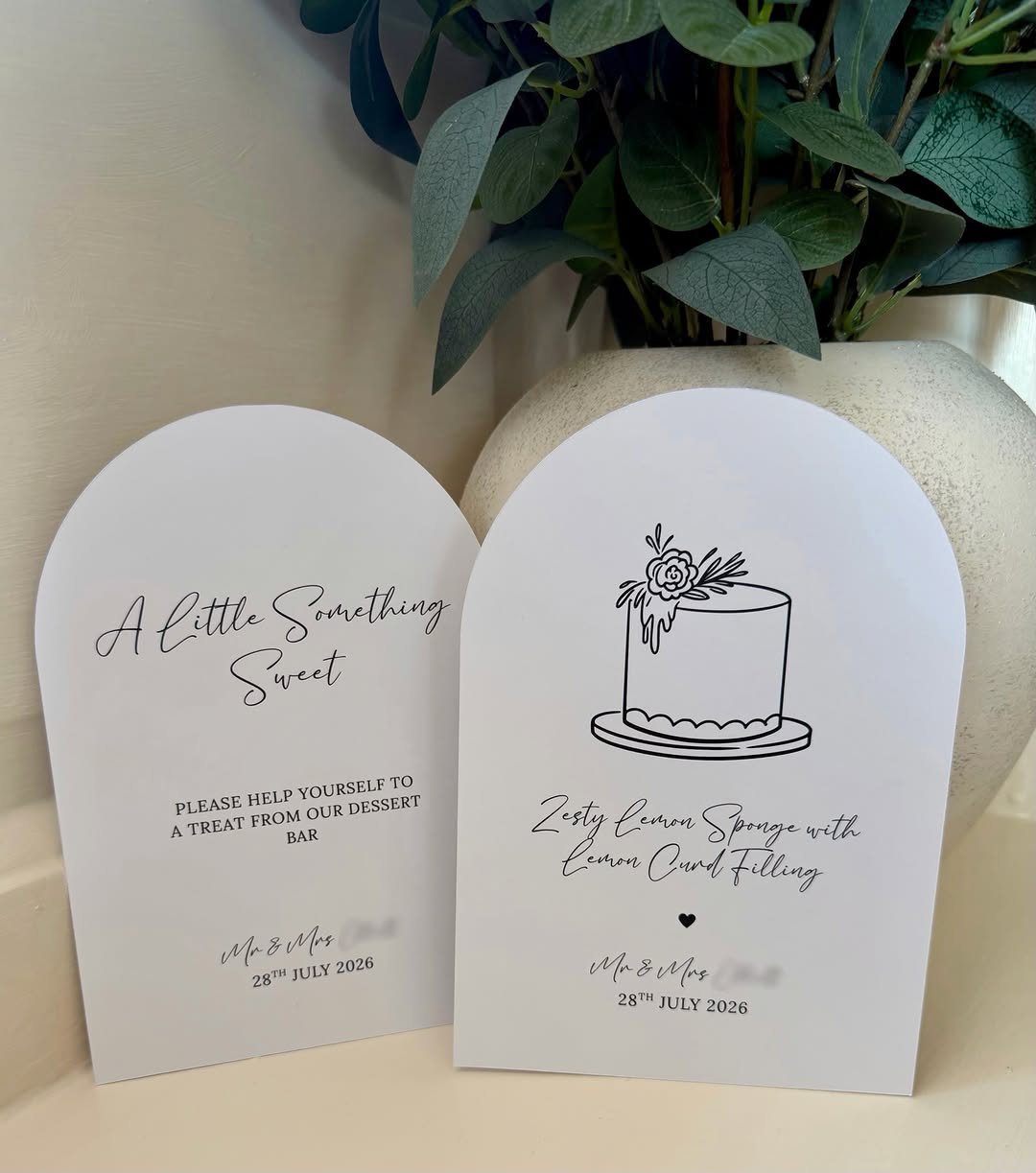 Two white arched dessert table signs with black calligraphy and a cake drawing.