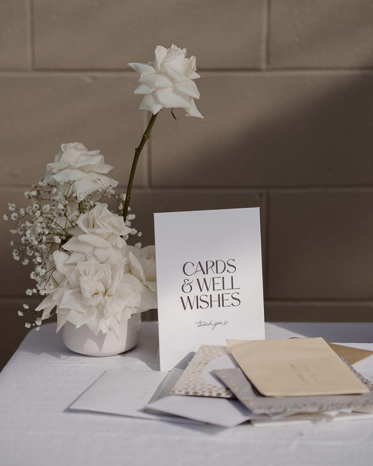 Cards and well wishes sign next to white roses and envelopes on a table.