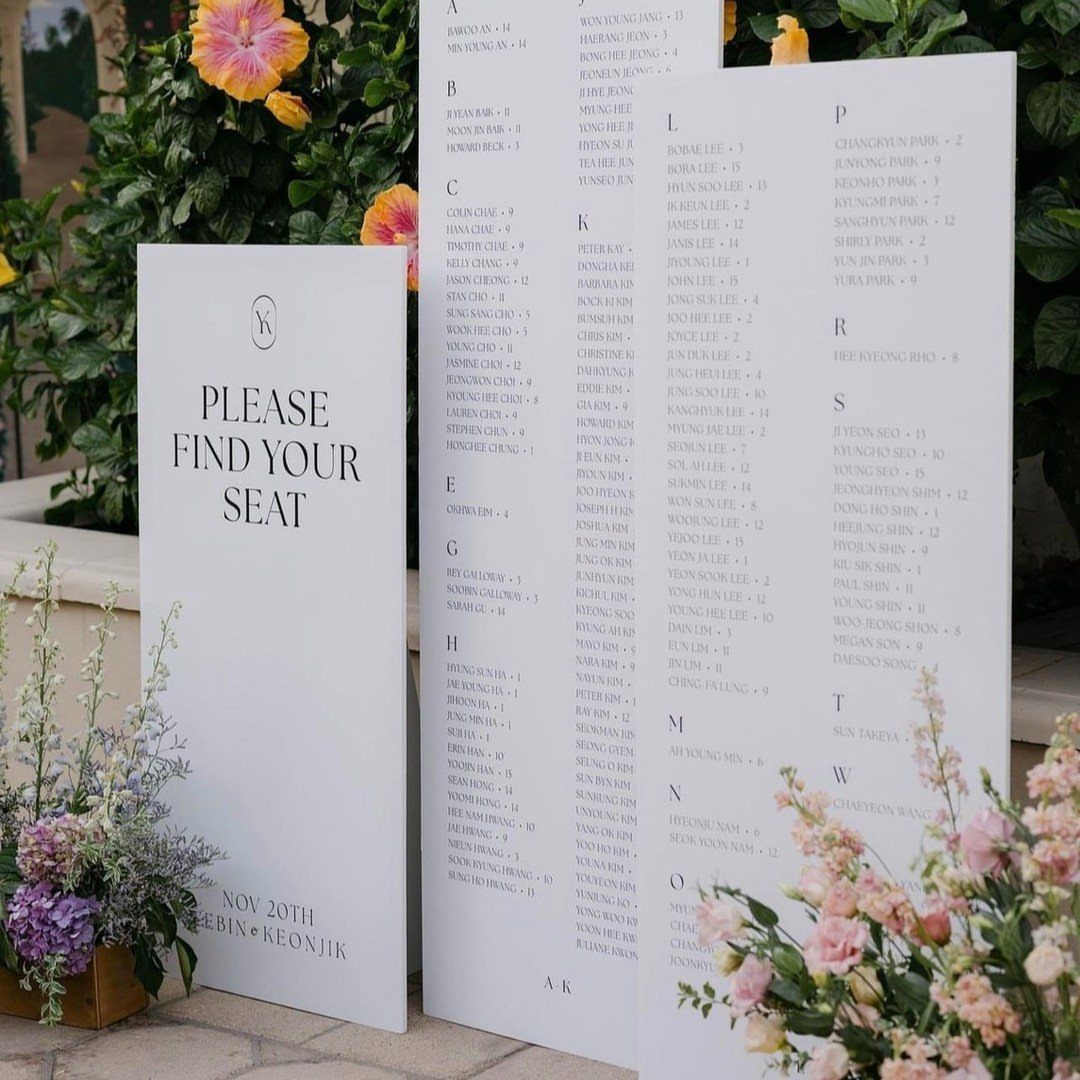 White wedding seating chart boards with guest names and table numbers in a garden.