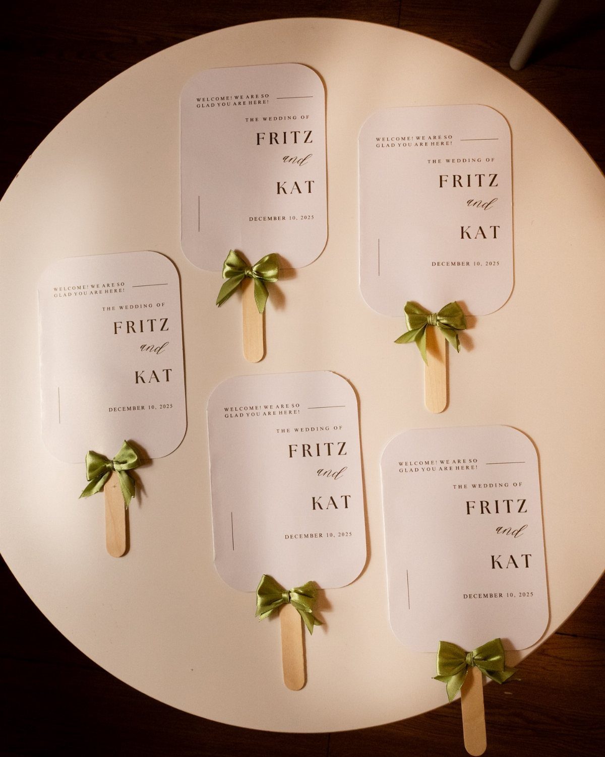 White custom wedding hand fans with green ribbons and wooden handles on white background