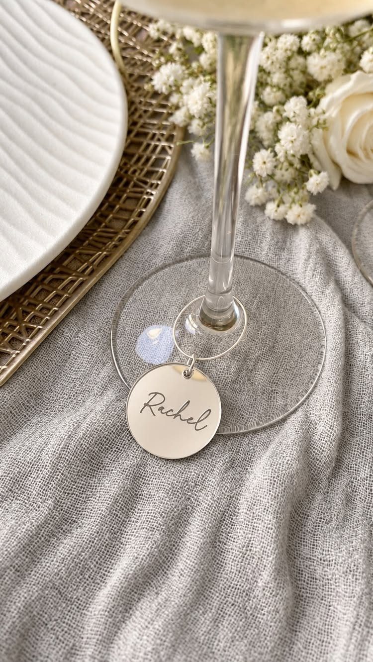 Gold circular drink charm engraved with Rachel hanging from a champagne glass stem