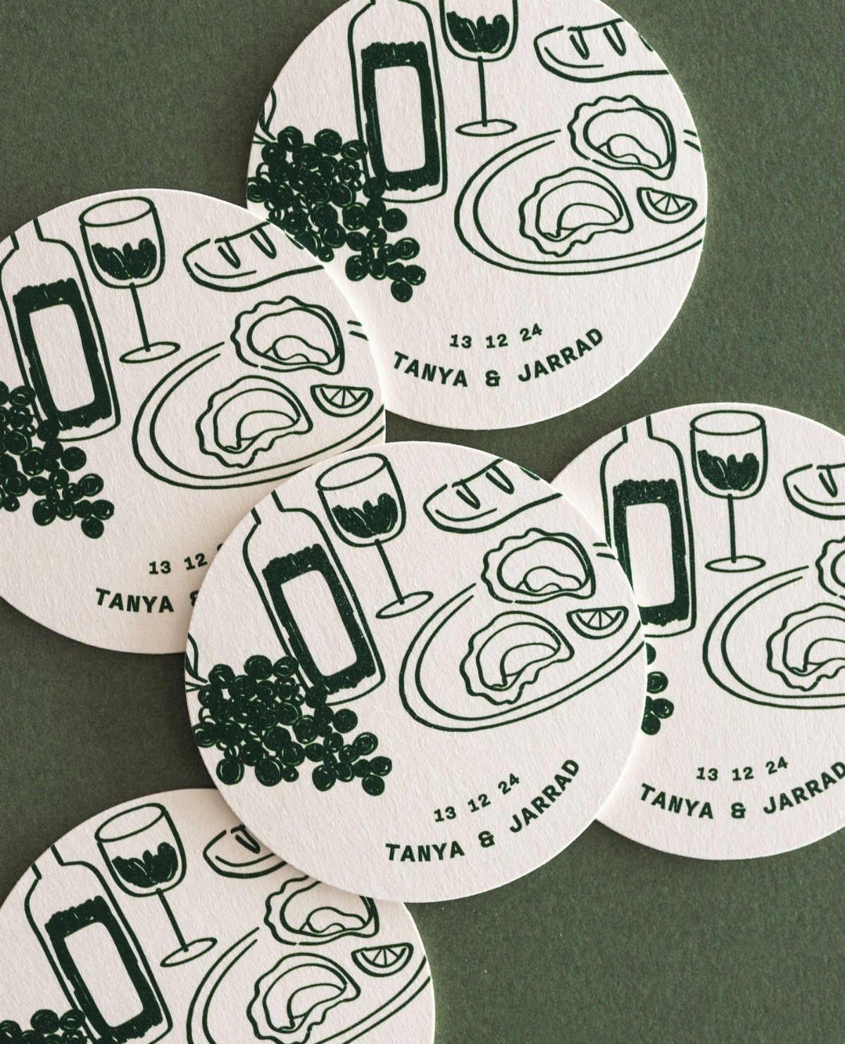 Circular white coasters with green illustrations of wine and oysters for a wedding.