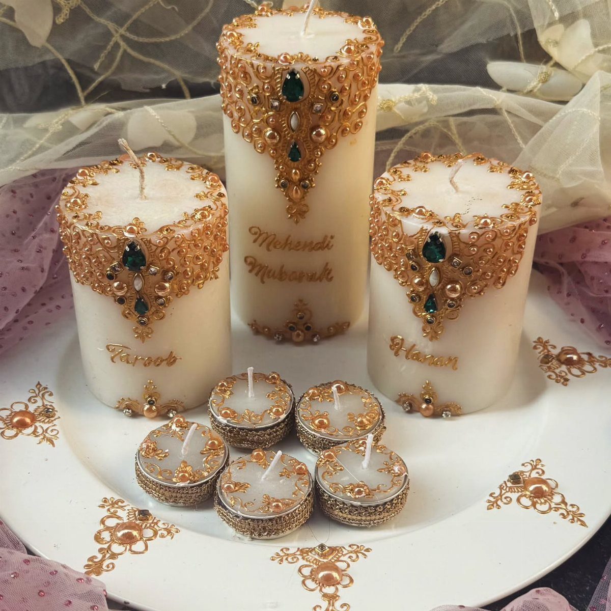 White pillar and tea light candles decorated with gold lace and green gemstones.