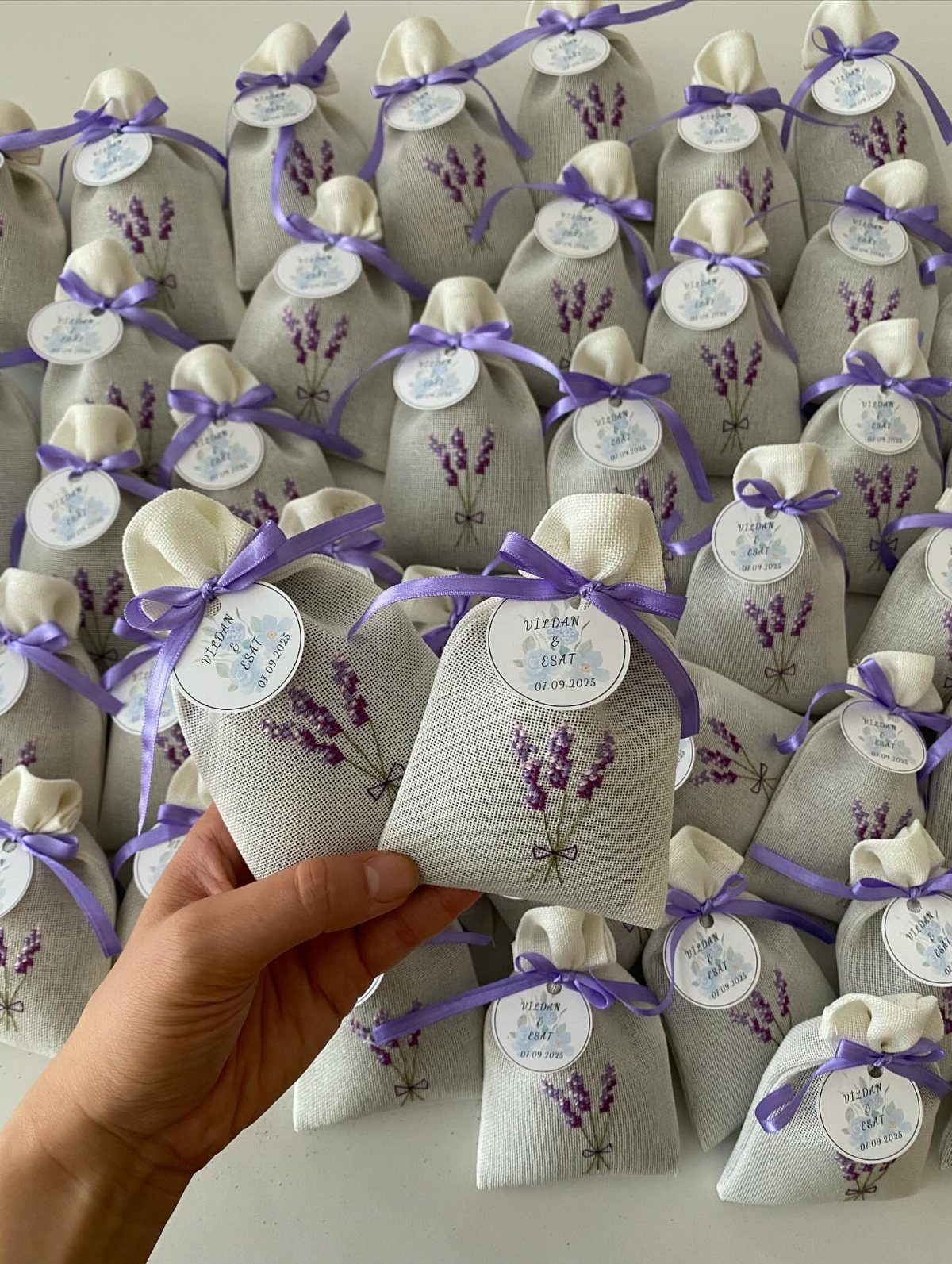 Grey linen lavender sachets with purple ribbons and personalized tags for wedding favors.