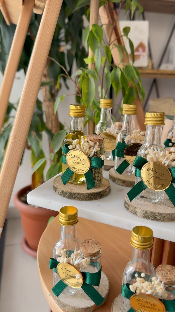 Small olive oil bottles with green ribbons and gold tags on wooden coasters.