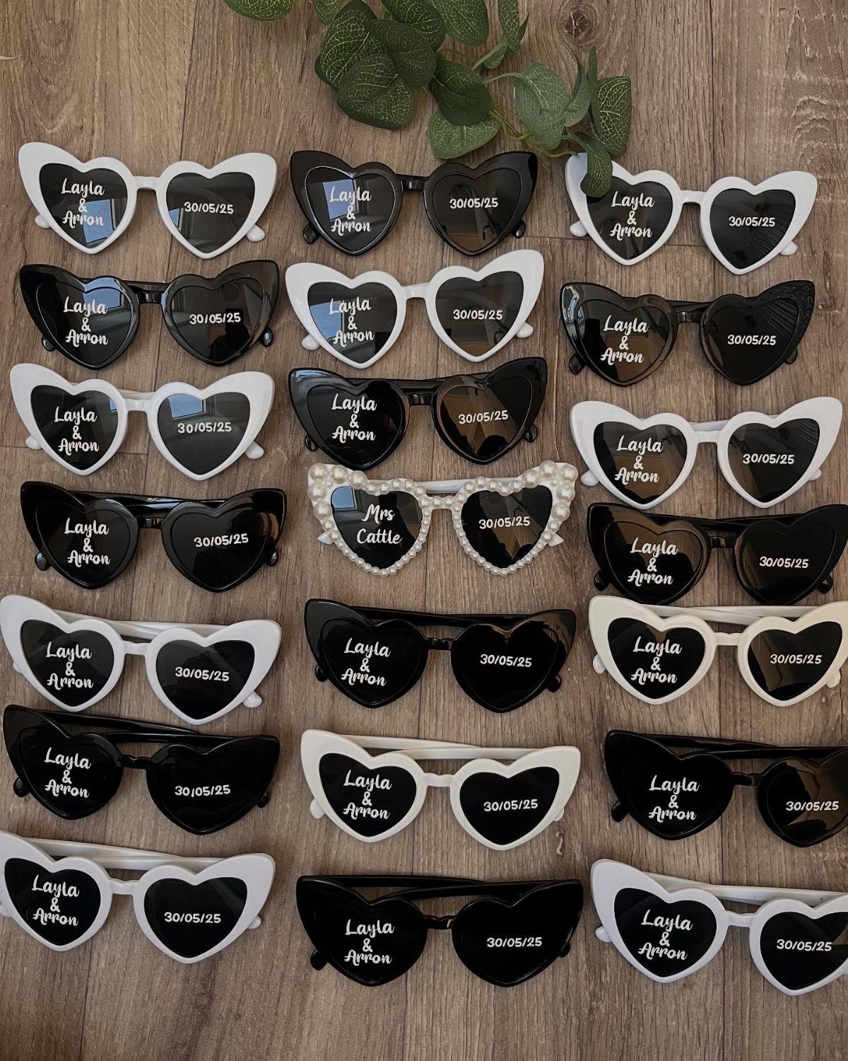 Heart-shaped sunglasses in black and white with personalized names and dates on lenses.