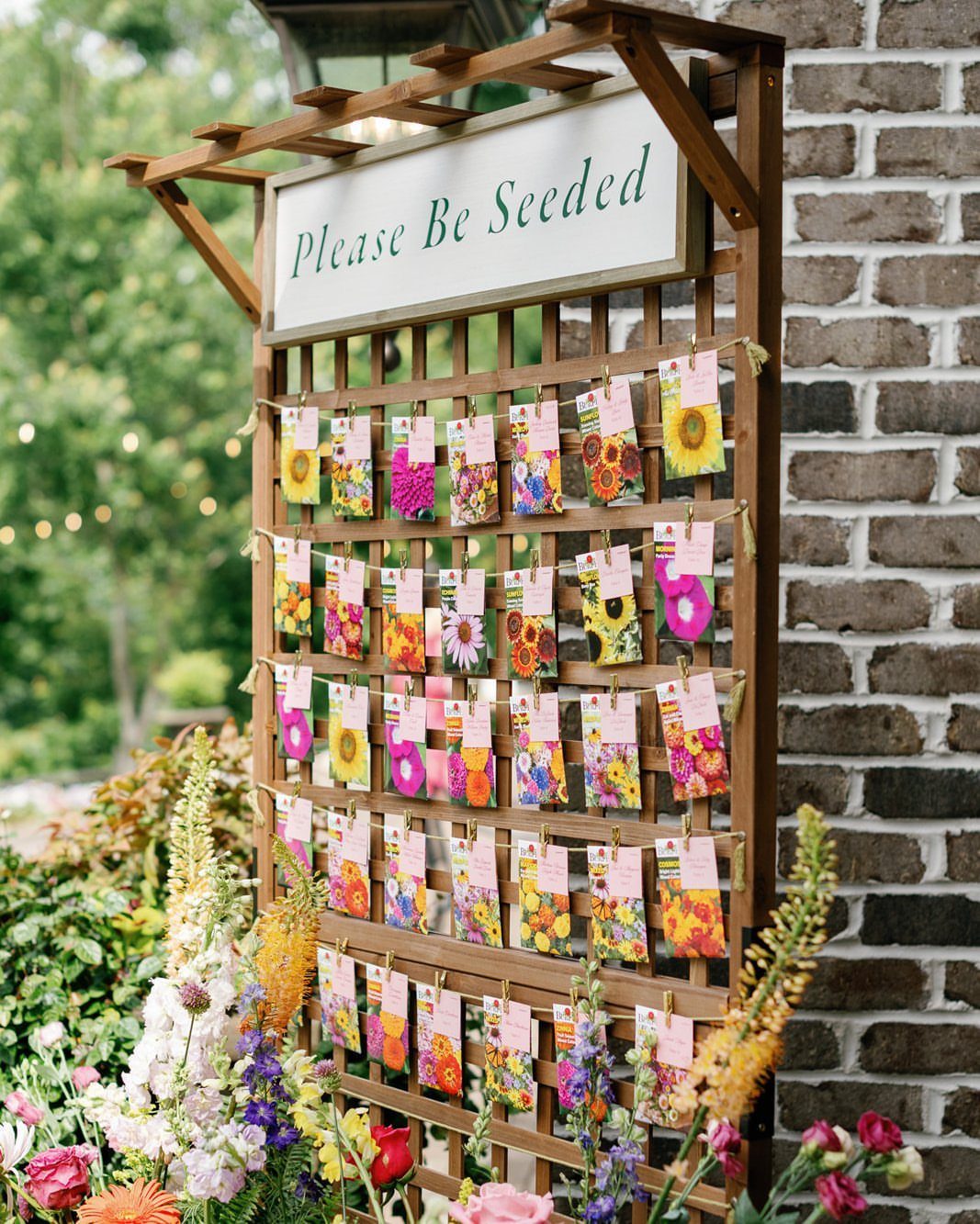 Seed packets hanging on a wooden trellis with a Please Be Seeded sign.