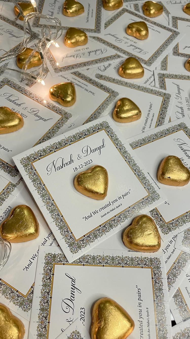 Gold heart-shaped chocolates on personalized white wedding favor cards with fairy lights.