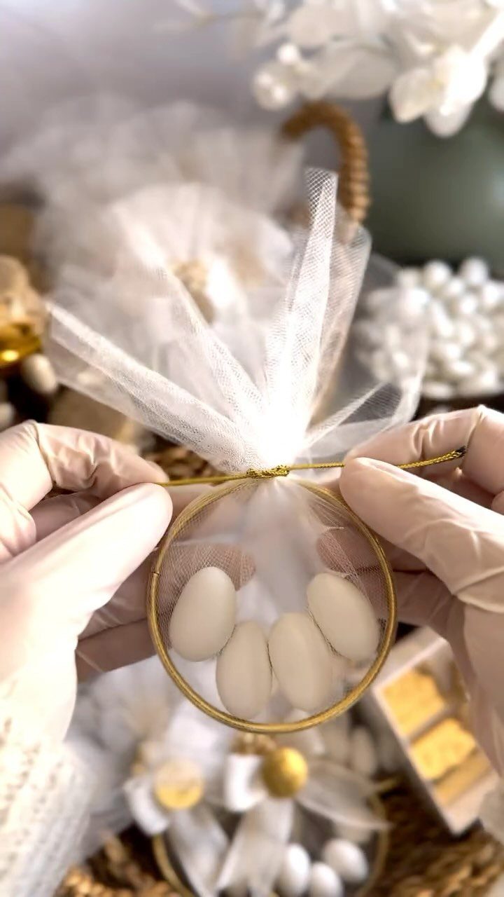 White tulle drawstring bag filled with white almond candies held by gloved hands.