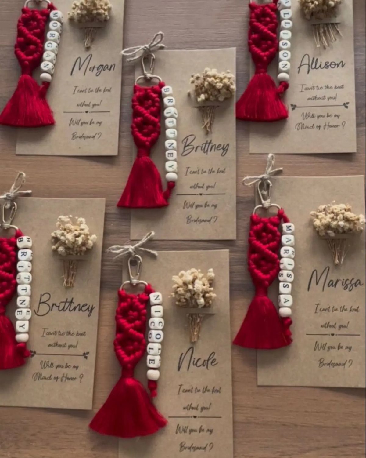 Red fabric dress keychains with name beads and dried flowers on personalized cards.