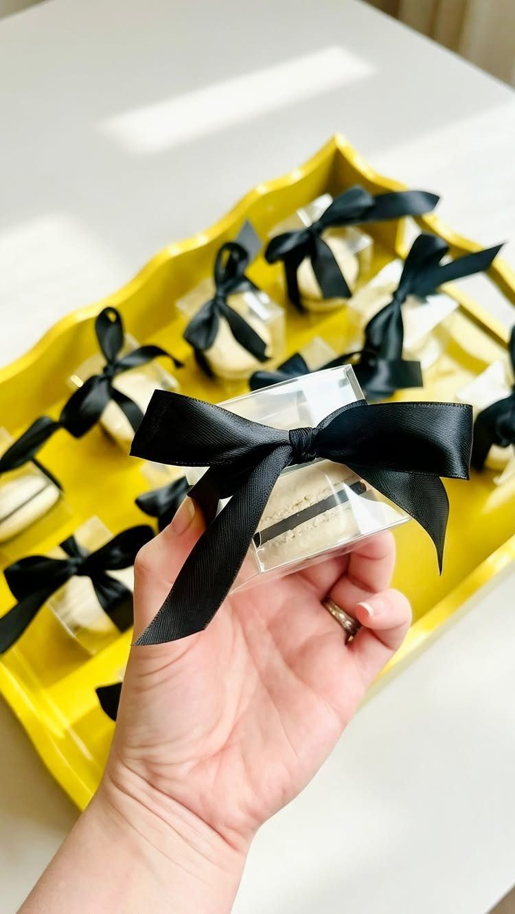 White macarons in clear boxes with black bows on a yellow tray