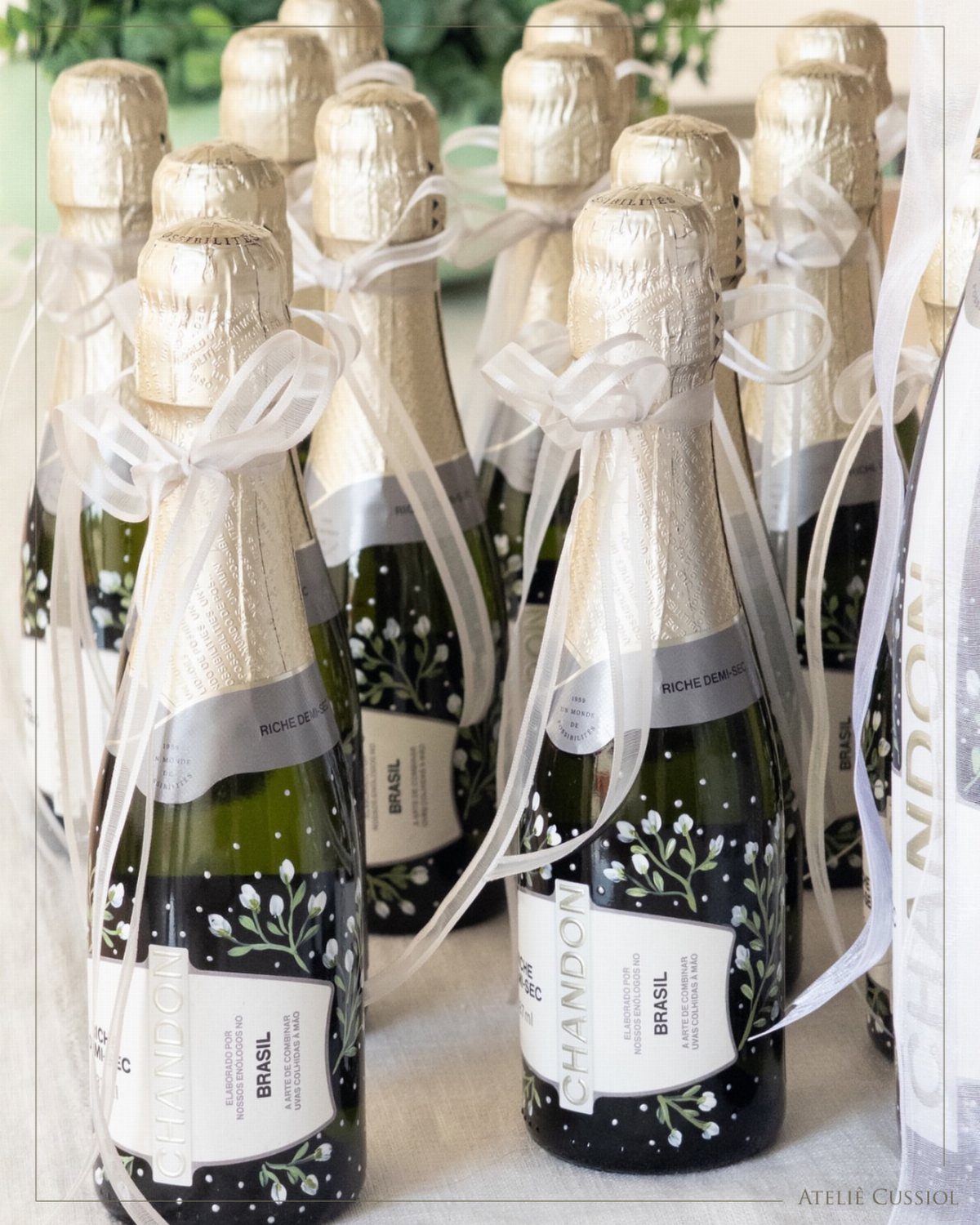 Mini champagne bottles with gold foil tops and white ribbons as wedding favors.