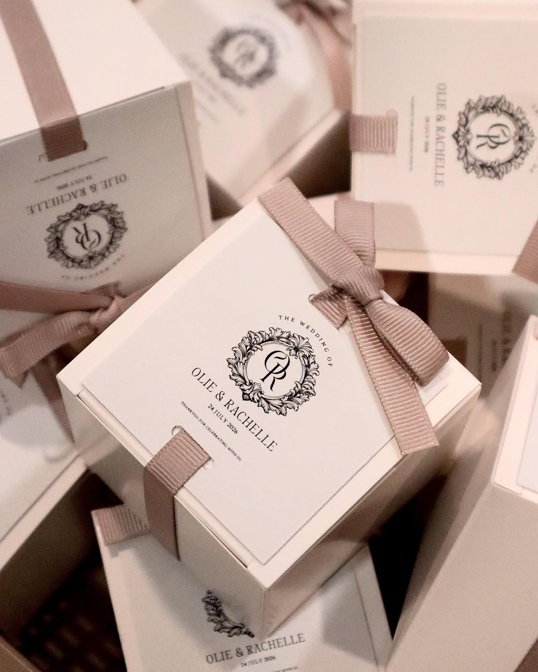 White square wedding favor boxes tied with pink ribbons and personalized black text.