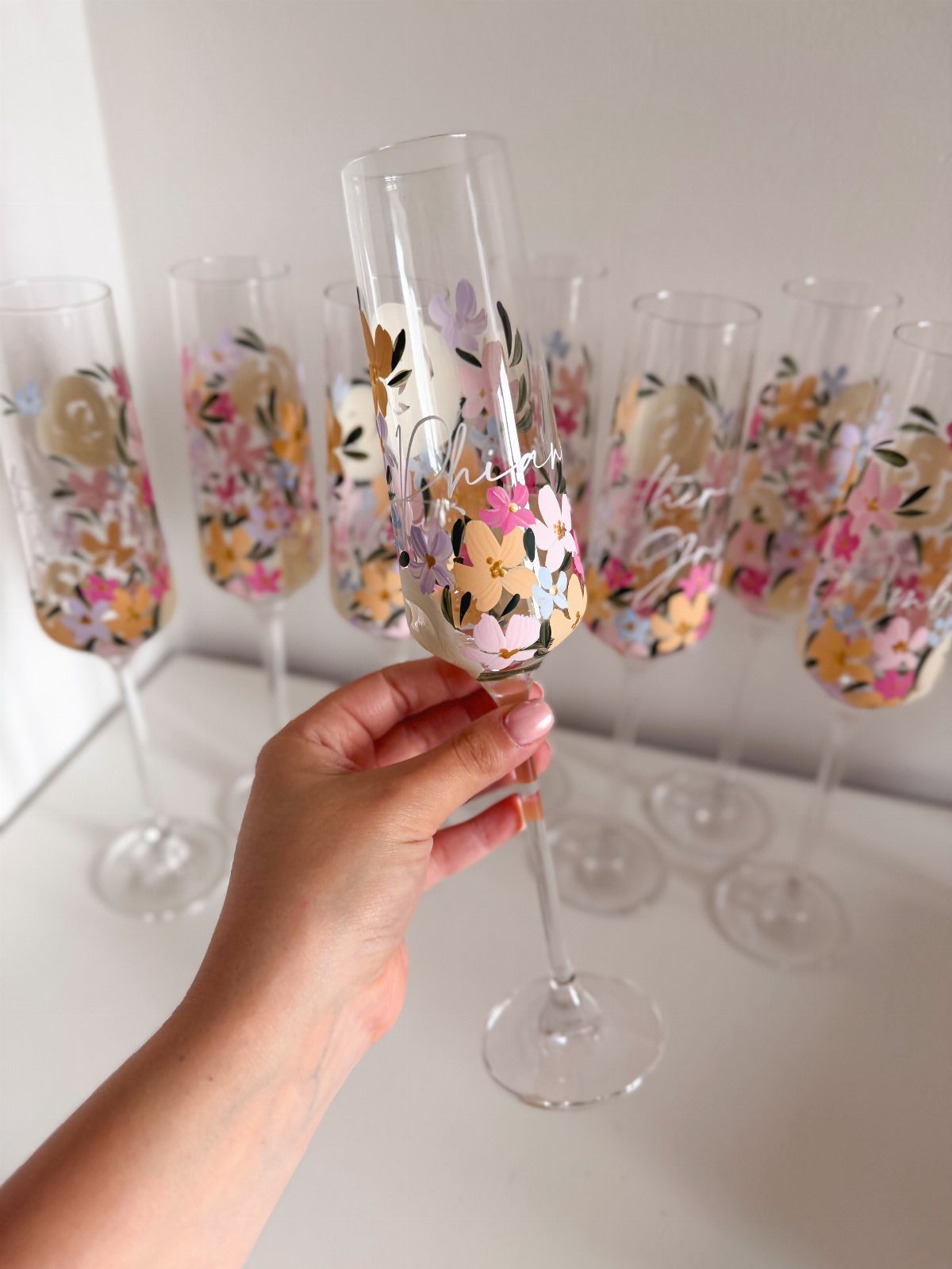 Personalized champagne flutes with colorful floral designs and names on a white background