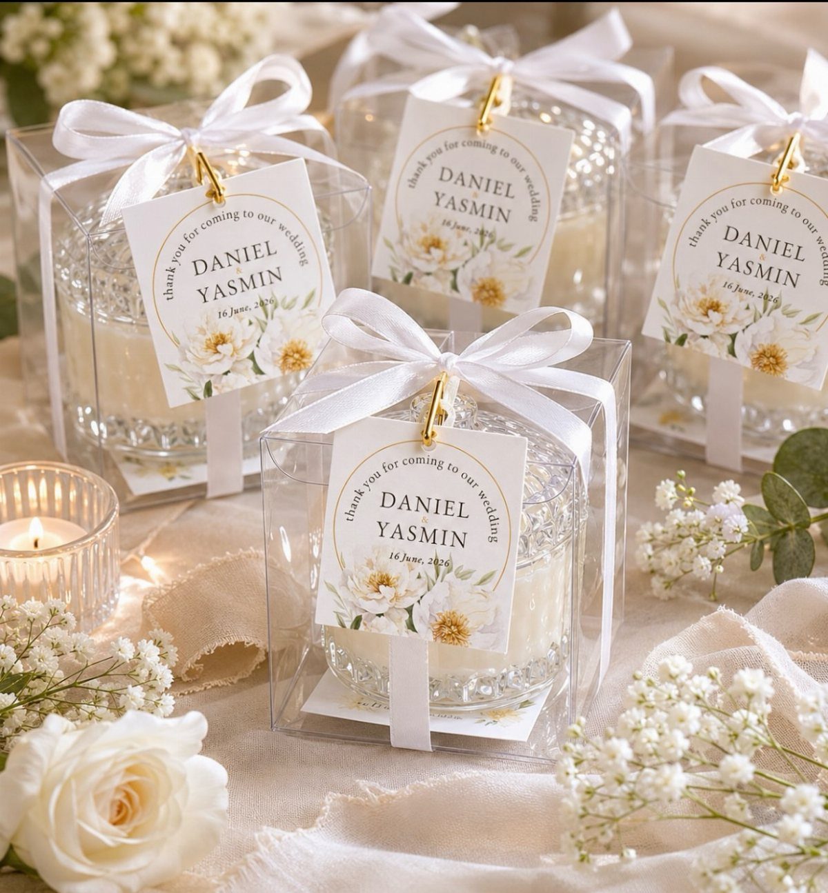 Small white candles in clear boxes with white ribbons and personalized wedding tags.