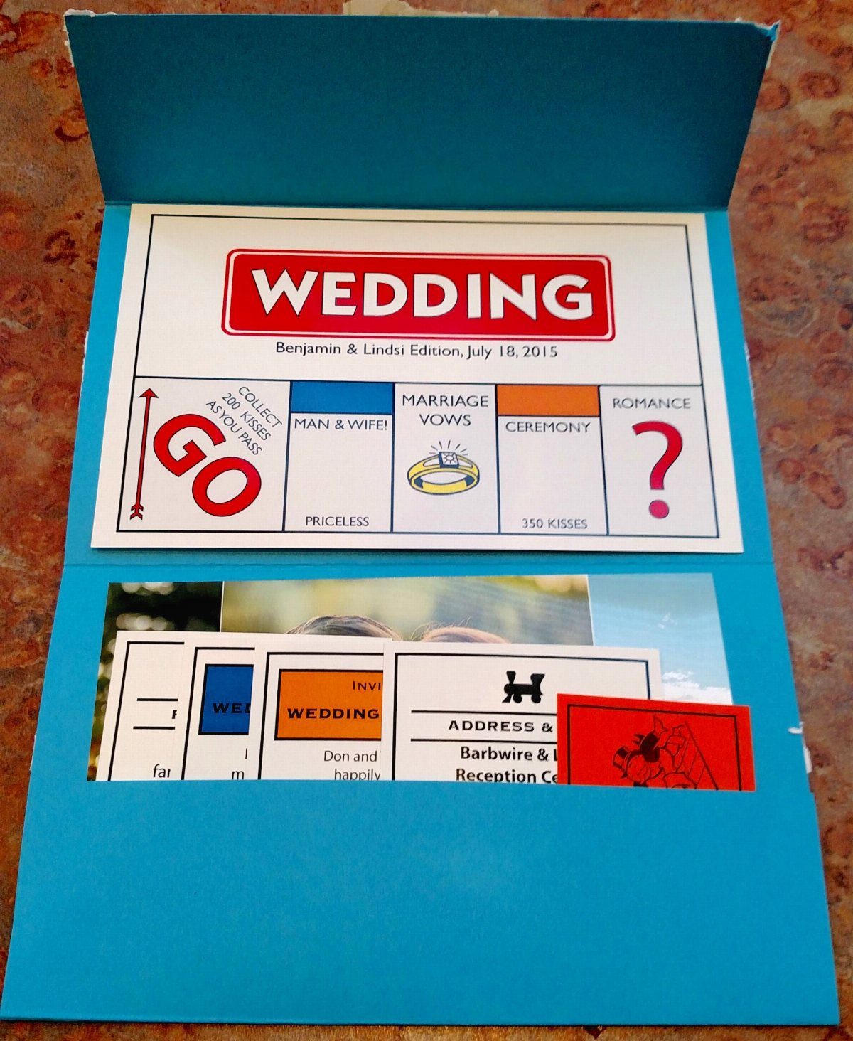 Monopoly board game themed wedding invitation with colorful cards in a blue folder