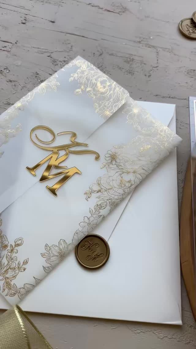 White wedding envelope with gold floral patterns, gold monogram, and gold wax seal.