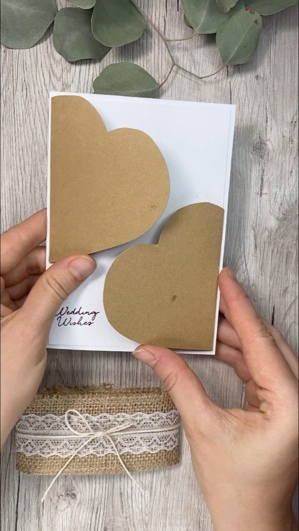 White wedding card with two brown kraft paper hearts held by two hands.