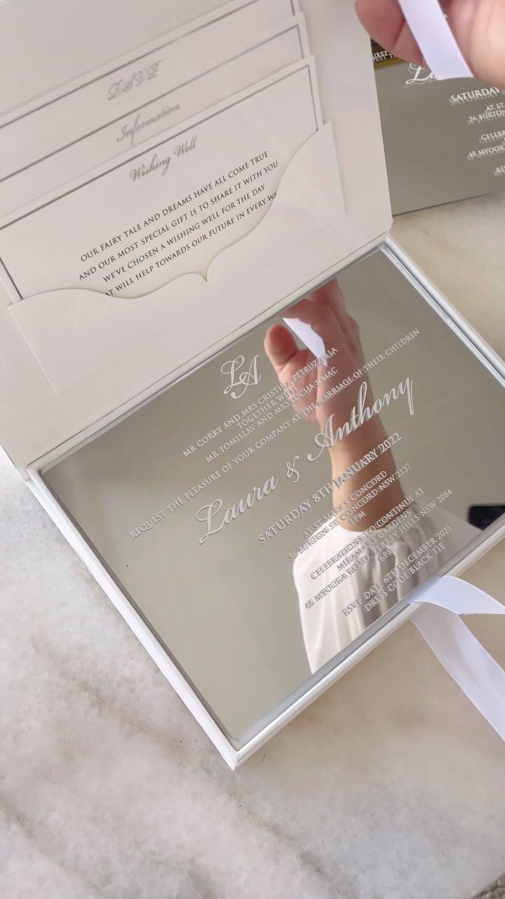 Mirrored wedding invitation with white calligraphy text and white interior cards.