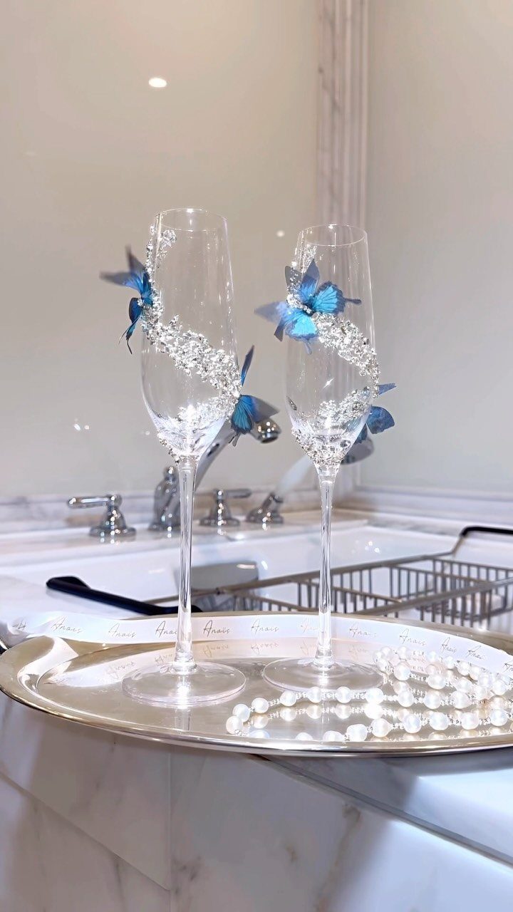 Two champagne flutes adorned with crystals and blue butterflies on a silver tray.