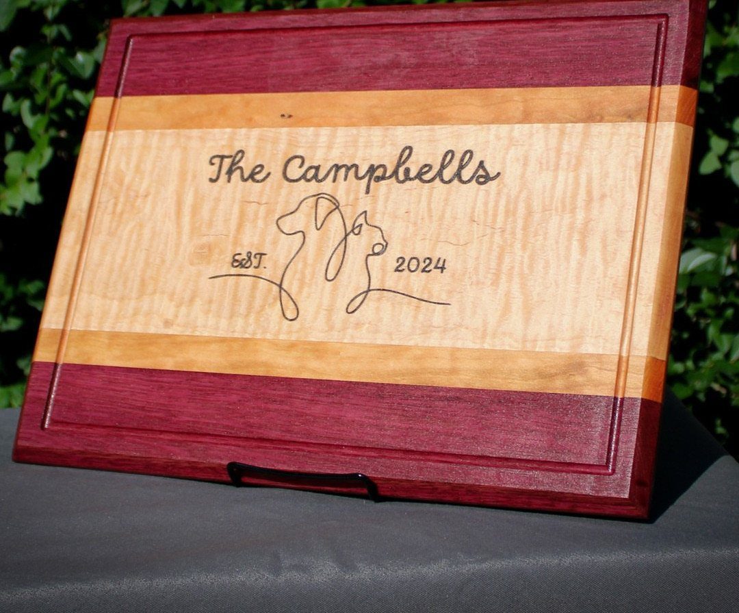 Engraved wooden cutting board with The Campbells name and two dogs line art.