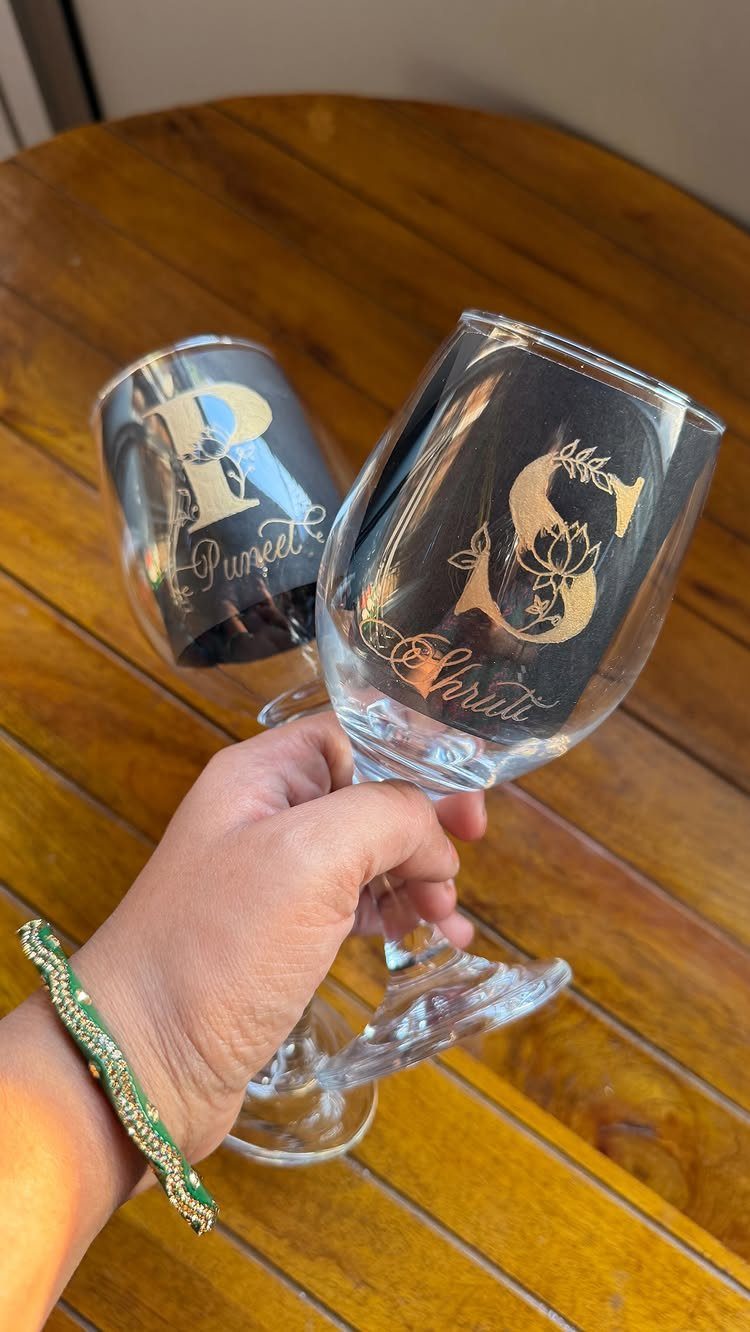 Two engraved wine glasses with gold initials held over a wooden table.