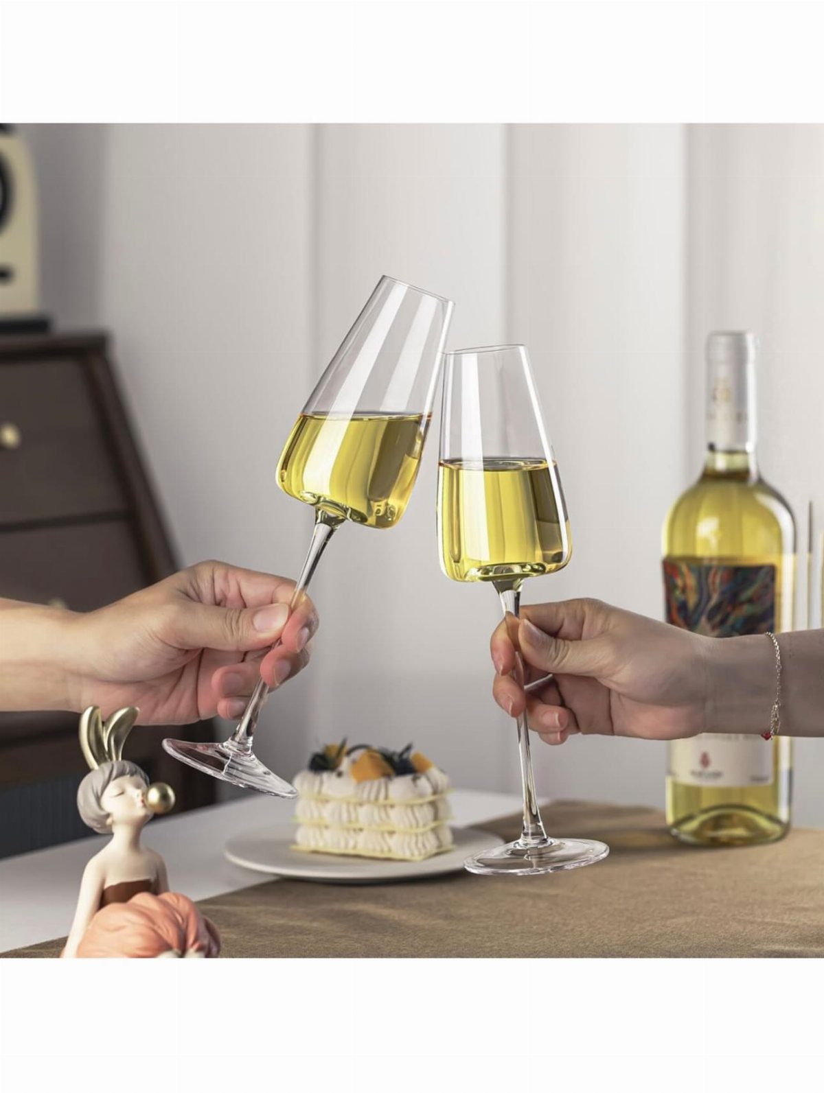 Heart-shaped wine glasses clinking with white wine on a table with cake.