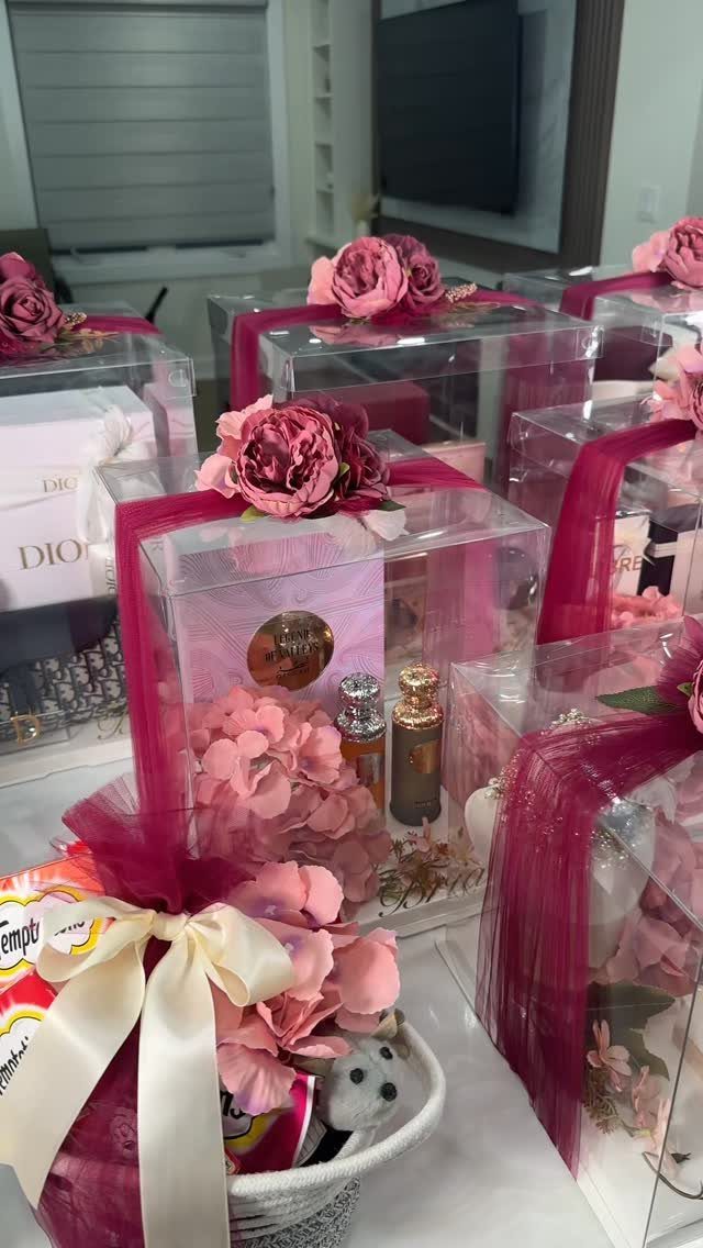 Acrylic gift boxes with pink roses, perfume, and ribbons on a white table.