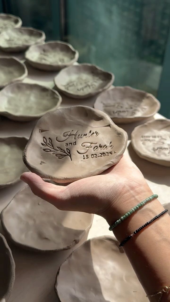 Handmade clay dish with stamped names and wedding date held in a hand.
