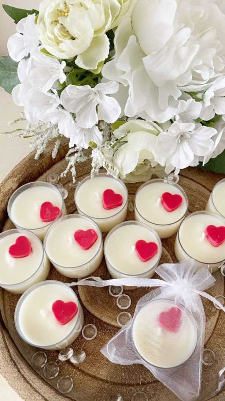 White candles with red heart toppers on a wooden tray with white flowers.