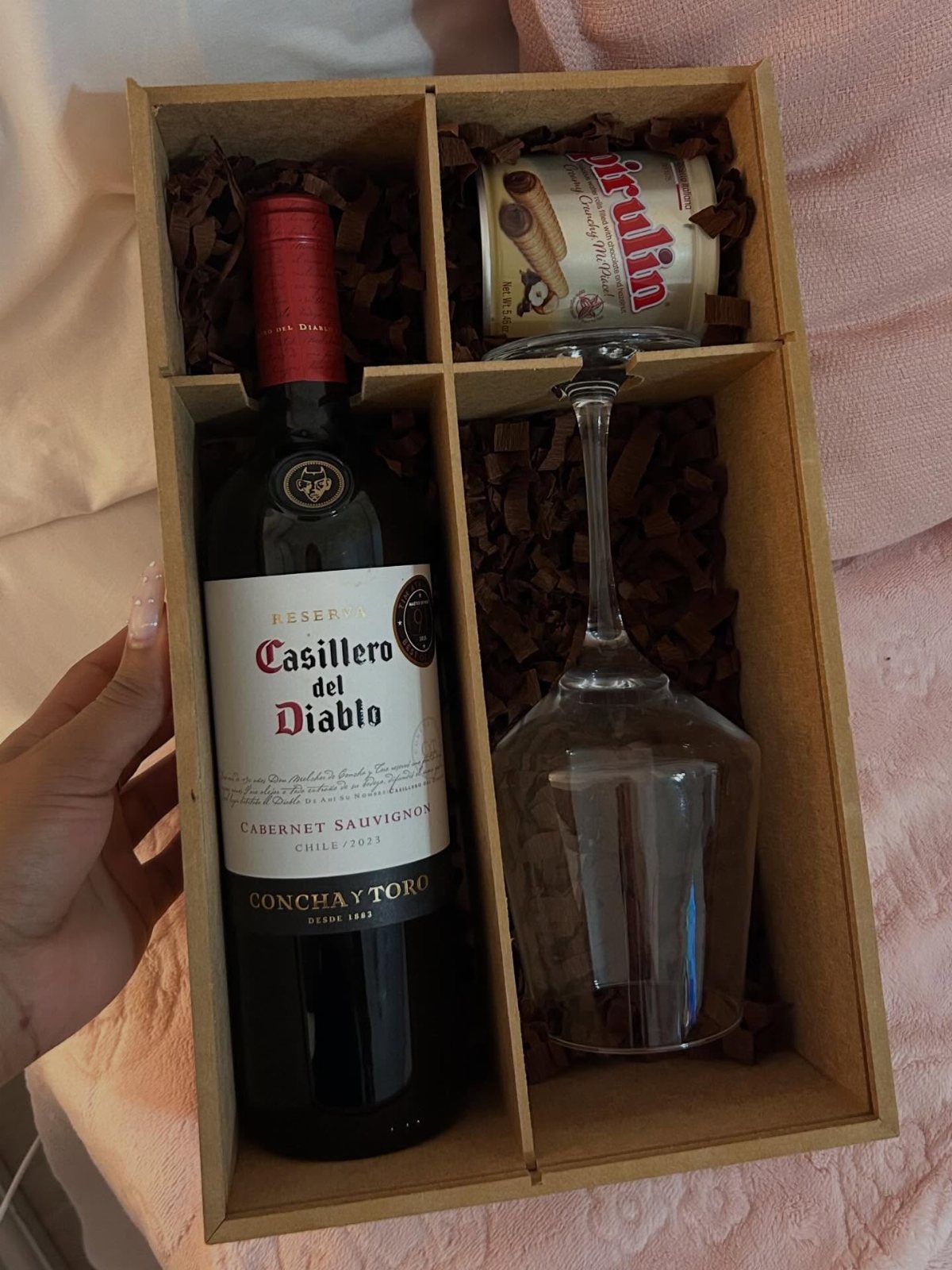 Wine gift box with red wine bottle, glass, and snacks in brown filler