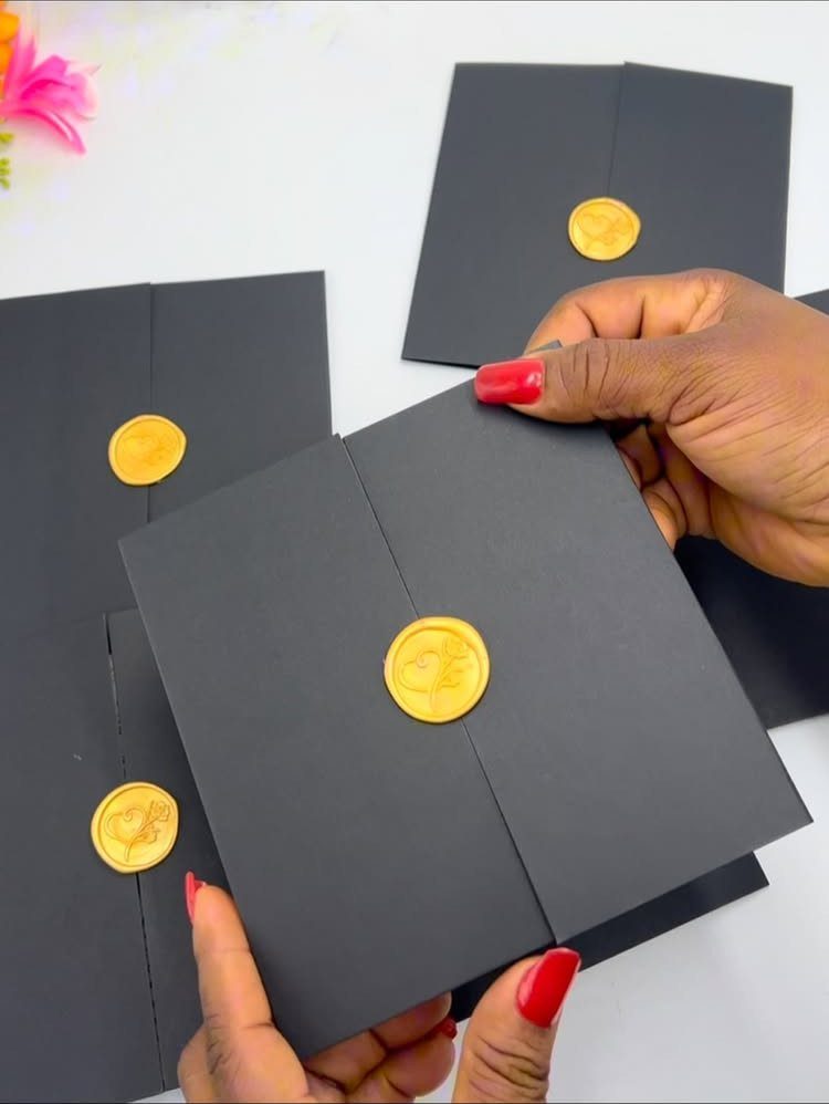 Black envelopes with gold wax seals held by hands with red nail polish.