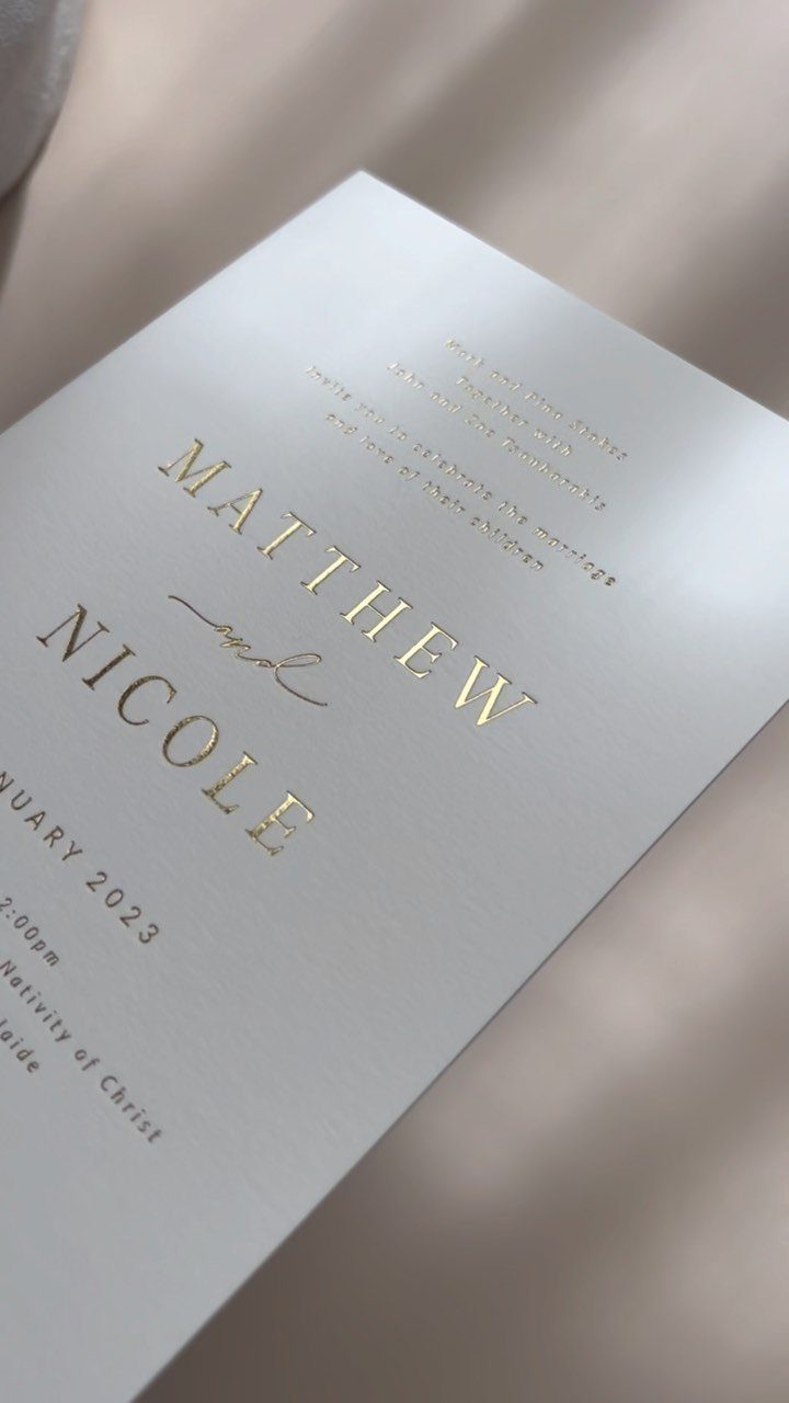 White wedding invitation with shiny gold foil lettering on a soft fabric background