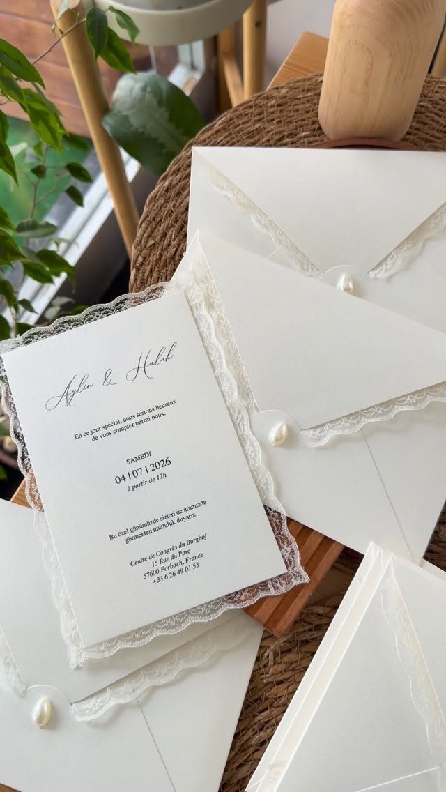 White wedding invitations with lace trim and pearl closures on a rustic surface.