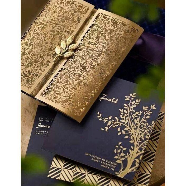 Gold laser-cut floral invitation sleeve resting on a navy blue gold-foiled card.