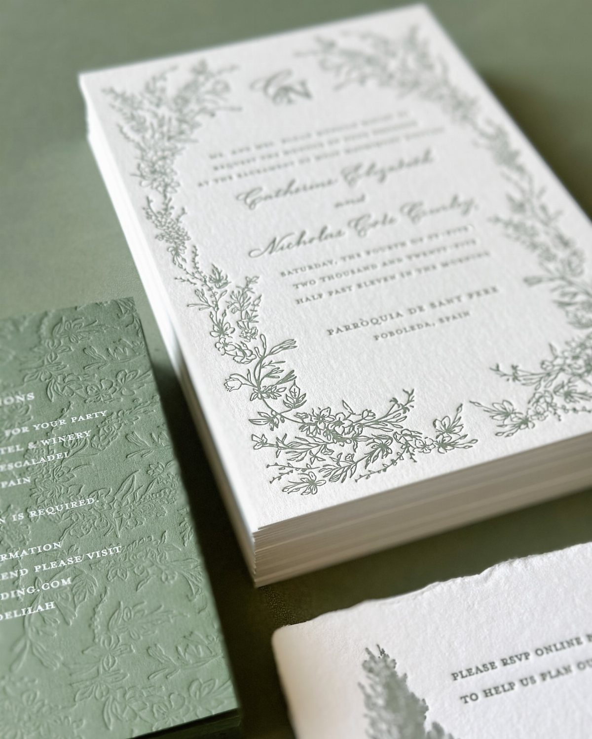 White wedding invitations with grey floral borders and elegant cursive typography on green background