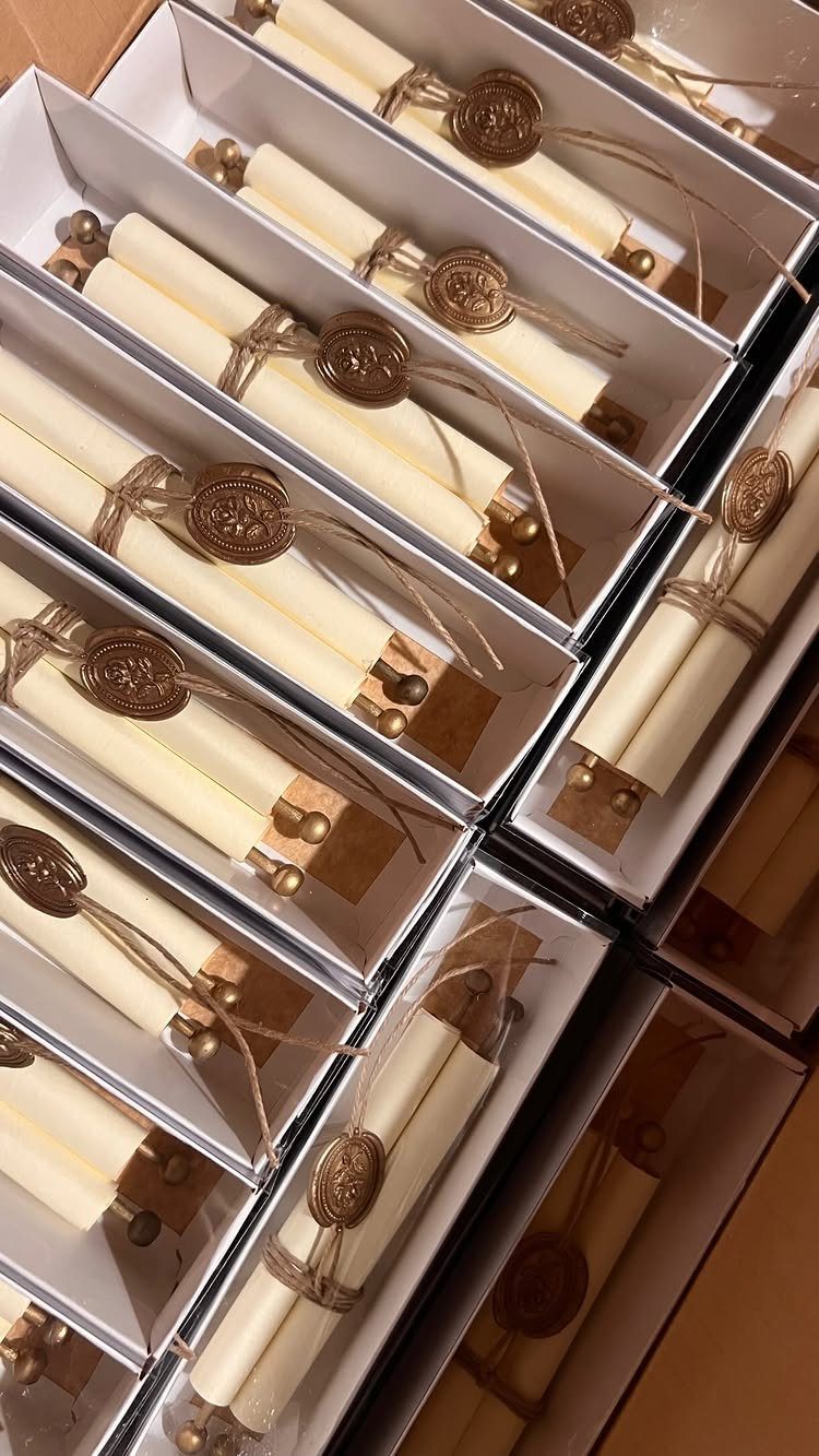Cream paper scrolls with gold wax seals and twine in white boxes.