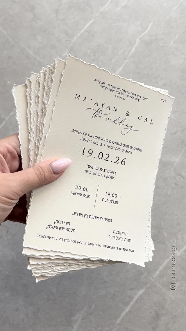 Stack of cream wedding invitations with deckled edges held by a hand.