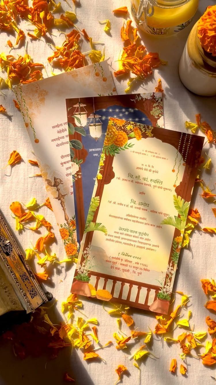 Indian wedding invitation cards surrounded by orange and yellow flower petals on white fabric.