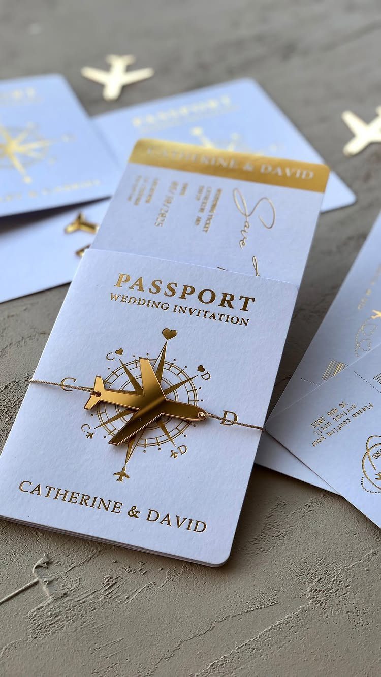 Passport-style wedding invitations with gold foil accents and a small gold airplane charm.