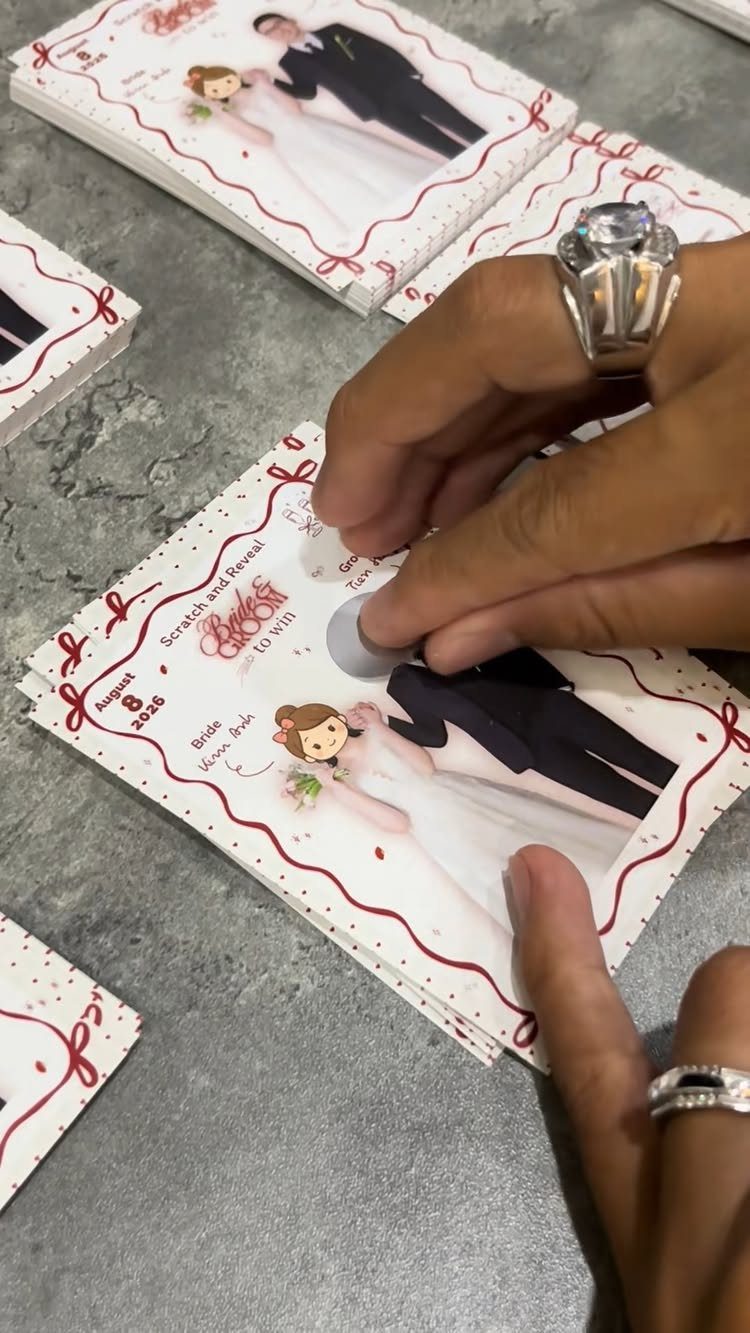 Hands scratching a personalized wedding scratch-off lottery ticket featuring a cartoon couple.