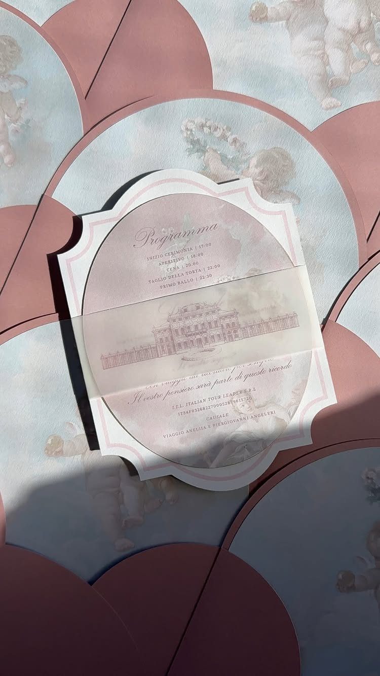 Scalloped circular wedding invitation resting on overlapping pink and blue curved paper shapes.