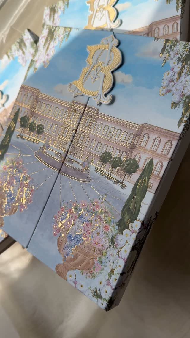 Illustrated wedding invitation featuring a grand estate, floral accents, and a gold letter B.