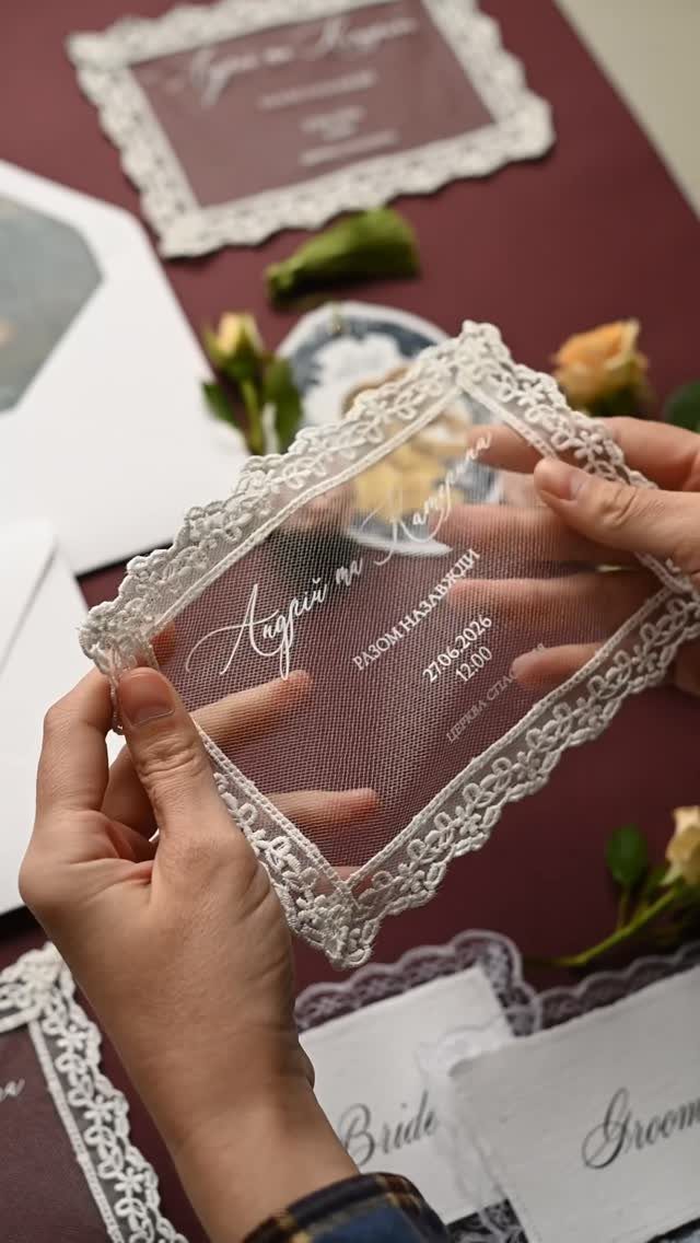 Transparent acrylic wedding invitation with white lace border held by two hands