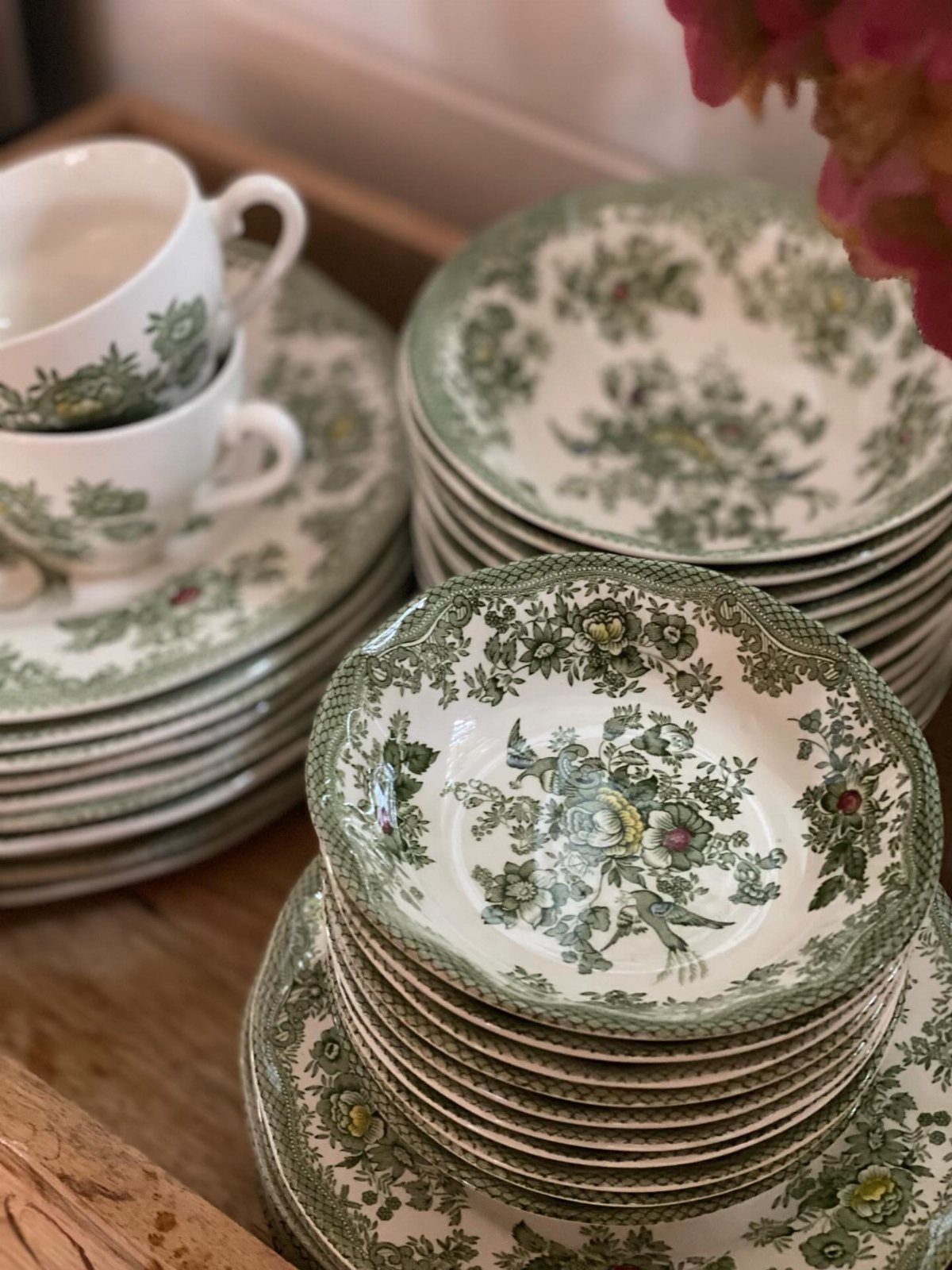 Stacks of white ceramic plates and bowls with green floral vintage patterns.