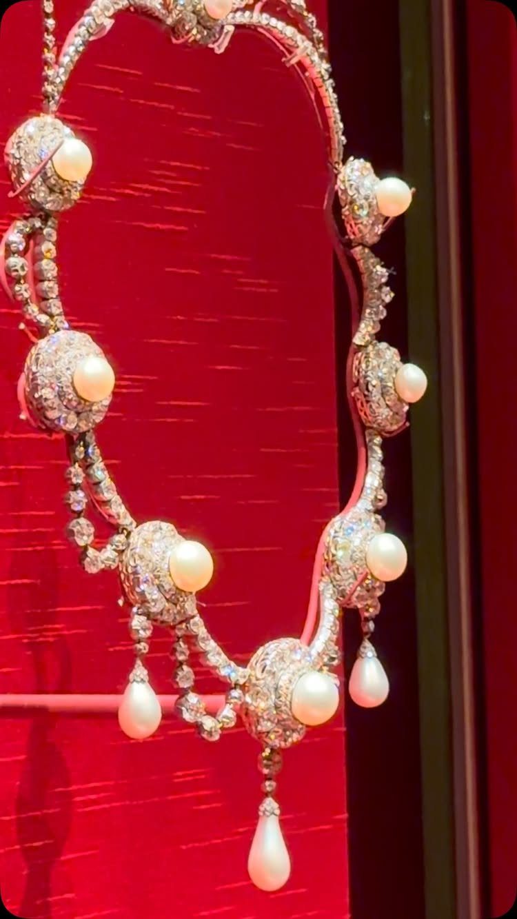 Ornate vintage diamond and pearl necklace displayed against a bright red background.